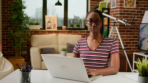 Portrait of female freelancer working remotely from home, using laptop and online connection to do business job in living room. Office employee doing startup remote work at desk.