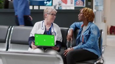 Woman and medic looking at greenscreen display on laptop in hospital reception lobby. Old physician holding computer with isolated chroma key template, blank mockup and copyspace.
