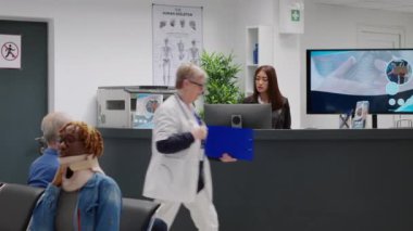 Diverse medical team working at hospital reception desk, giving assistance to patients in waiting room area on seats. Nurse and receptionist helping people in lobby, private healthcare center.
