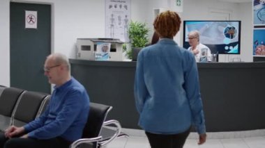 Receptionist and physician looking at computer behind facility reception desk to work on healthcare appointments and medical consultation. Waiting room area checkup visit at clinic.