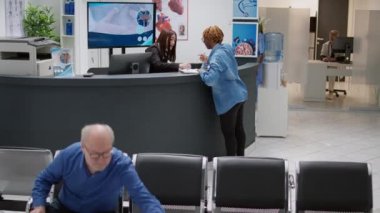 African american patient filling in checkup report at reception counter, receiving help from asian receptionist. Woman having medical consultation appointment, waiting area lobby.