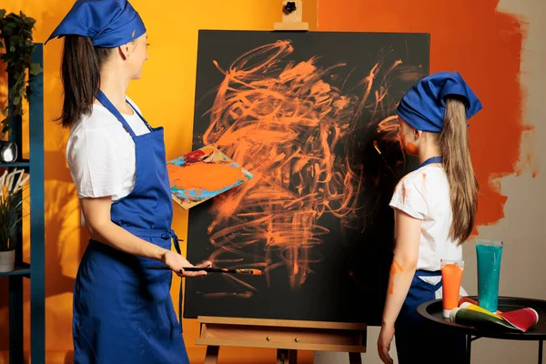 Artists family painting artwork on canvas, using mixing tray with aquarelle watercolor and wet dye to create masterpiece design. Learning new artistic skills to paint with paintbrush.