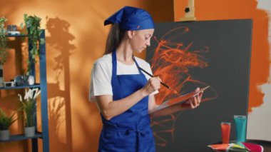 Portrait of female artist painting masterpiece on canvas, using watercolor and aquarelle palette with orange color to paint professional artwork. Creating design with artistic skills and vision.