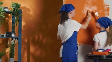 Mom and kid playing with orange paint and renovating house, painting apartment walls with color and paintbrush. Getting dirty and messy with paint, diy housework redecoration. Handheld shot.