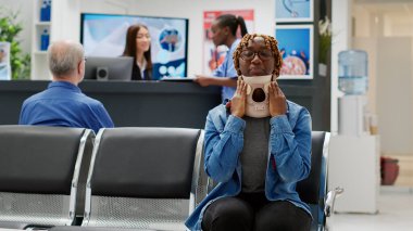 Portrait of african american patient with cervical neck foam waiting to attend checkup consultation with specialist, trying to cure accident injury. Person with medical collar brace. Handheld shot.