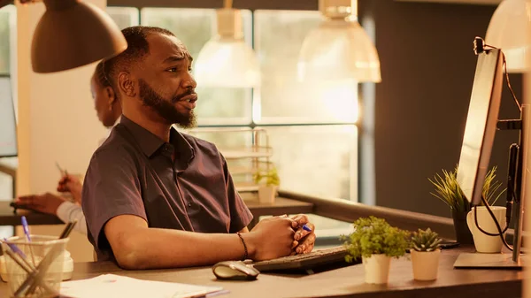 Business man waving at videocall meeting webcam on computer, talking to coworkers on internet network. Using online videoconference and remote teleconference call during sunset. Tripod shot.