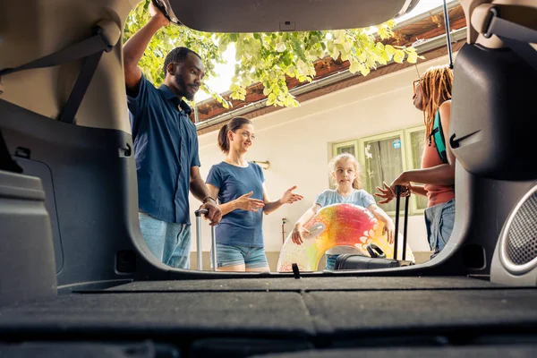 Diverse family and friends travelling on holiday with vehicle, going on summer vacation. Little girl with mother and young couple leaving with automobile on road trip journey, adventure.