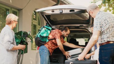 Family loading voyage baggage and trolleys inside car trunk while going on summer vacation citybreak. Casual people going on holiday field trip while putting luggage inside vehicle.