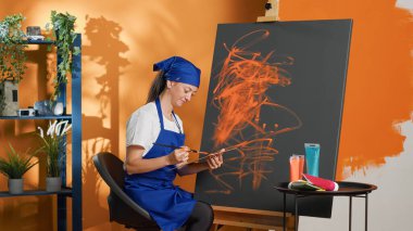 Female painter using aquarelle color to create art design on canvas, painting artistic masterpiece with paintbrush and watercolor palette. Doing artwork with skills and vision. Tripod shot.