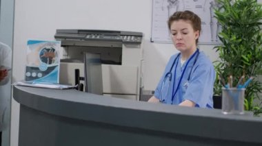 Medical assistant working at hospital reception desk in facility, helping people with healthcare appointments and checkup visits. Female nurse using report papers for consultation at health center.