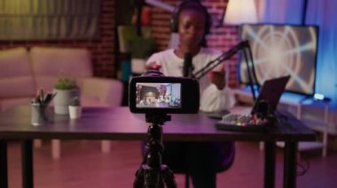 Selective focus on digital video camera screen recording african american vlogger talking to audience from home podcasting studio. Influencer filming herself doing live broadcast for social media.