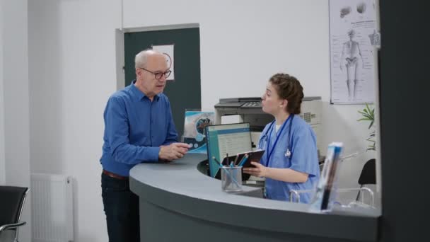 Medical Assistant Giving Insurance Support Old Patient Hospital Reception Desk — Vídeo de stock