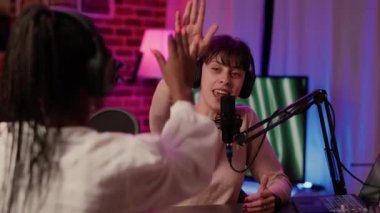 Selective focus on online radio host doing high five hand gesture with african american singer during live podcast in home studio. Portrait of influencer with headphones high fiving while recording