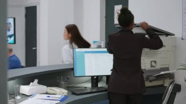 African american receptionist working at clinic registration desk with medical reports and checkup papers to help with appointments. Hospital worker giving insurance support at facility.