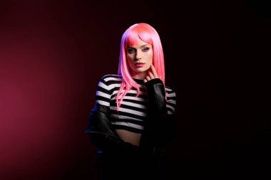 Confident pretty girl with pink hair looking at camera, expressing natural emotions and rocker punk fashion style. Wearing biker leather jacket with funky hairstyle, feeling modern and stylish.