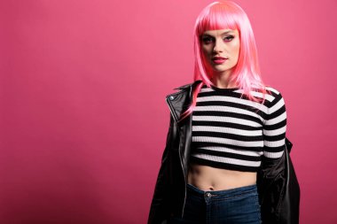 Portrait of trendy woman wearing stylish leather jacket in studio, feeling carefree and sensual with punk rocker style. Having pink hair and being funky, glamour amazing fashion over background.