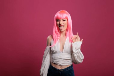 Portrait of stylish punk woman doing rock sign and sticking tongue out, showing aggressive hipster devil gesture. Cool female rocker advertising funky heavy metal symbol, fooling around.