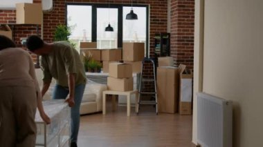 Married couple decorating new household with furniture after moving in together. Unpacking things in rented apartment space, relocating in family flat to start new beginnings on moving day.