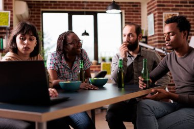 Multiethnic group of friends sitting at home together while watching drama movies on laptop computer. Diverse people sitting at table in living room while enjoying leisure activity.