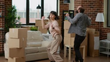 Life partners doing funky dance moves and feeling happy about moving in new household, celebrating relocation and home investment. Fooling around feeling playful in rented flat. Handheld shot.