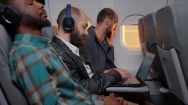 Businessman passenger using laptop computer on flight, travelling on work trip with tourists. Flying in economy class and working on device with online internet, sitting on airplane. Handheld shot.