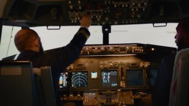 Diverse team of airliners turning on switch and buttons in cockpit using dashboard command. Pressing control panel power to fly airplane with windscreen, radar compass and engine. Handheld shot.