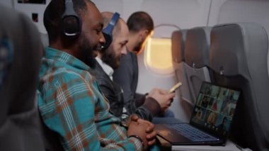 Entrepreneur talking on videocall conference on airplane flying in economy class. Using online remote teleconference call on laptop, travelling with internet meeting. Handheld shot.