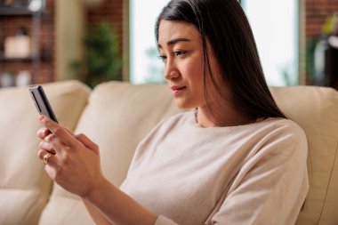 Normal görünümlü mutlu Asyalı kadın evde akıllı telefon kullanıyor, internet teknolojisi akıllı telefon kullanıcısı cep telefonu kullanıcı cep telefonu sosyal medya iletişim dijital aygıtı