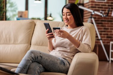 İnternetten alışveriş yapan Asyalı bir kadın, kredi kartıyla alışveriş yapıyor, akıllı telefon kredisi kullanıyor, mutlu bir kadın internet üzerinden ödeme yapıyor, internet üzerinden ödeme yapıyor, müşteri Asya uygulama ödemesi yapıyor.