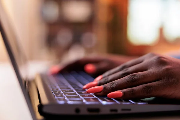 Female copywriter typing message on laptop keyboard, closeup on manicured nails. Young african american SMM manager browsing internet, writing email on computer, focus on hands