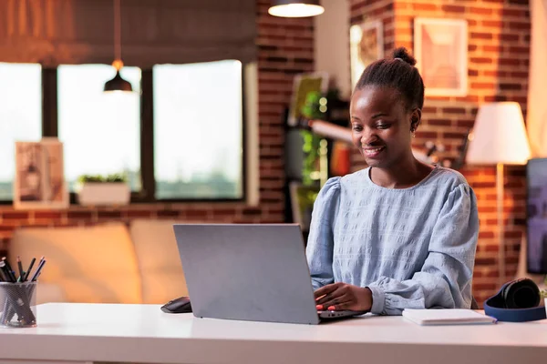 Female african american remote student typing on laptop and browsing internet in modern home office. Smiling female freelance copywriter using portable computer in coprorate workspace