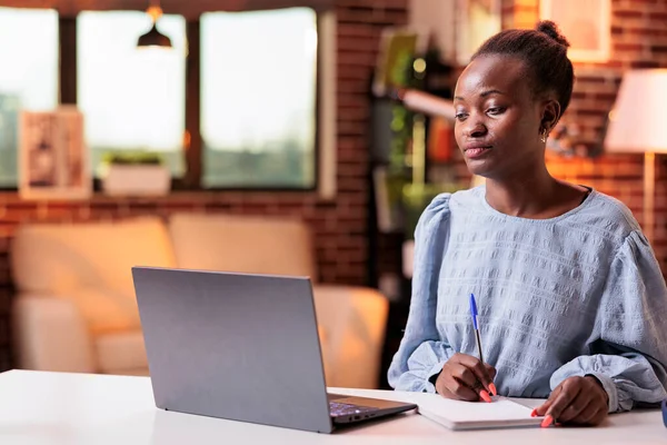 Remote school african american female student taking notes in notebook and studying with laptop at home. Internet courses tutorial watching, online education and modern e learning concept