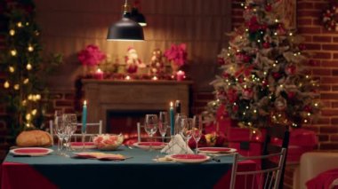 Empty traditional Christmas dinner table inside decorated living room with holiday garlands and dinnerware. Interior of traditional and authentic season cozy setting celebrating religious event.