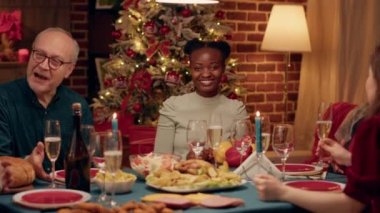 Cheerful family member feeling good while celebrating winter holidays with loved ones. Young african american woman smiling heartily at camera while enjoying Christmas dinner with close relatives.