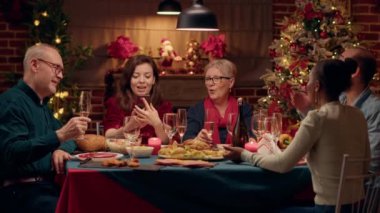 Beautiful happy wife presenting Christmas dinner to friend through smartphone internet video call. Festive diverse family members on cellphone online call with relatives wishing them Happy Holidays.