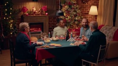 Lovely housewife bringing main course to Christmas dinner table. Impatient and happy festive family members gathered inside cozy home decorated with Xmas ornations while celebrating winter holiday.