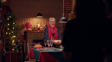 Joyful senior married couple welcoming guests to Christmas dinner at home. Festive people gathering in authentic Xmas decorated dining room to celebrate winter holiday with traditional food.