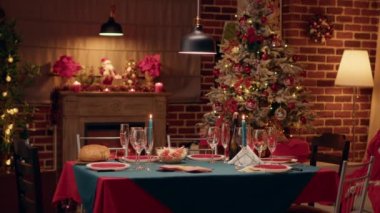 Empty interior of festive and ornate Christmas dinner table in living decorated with traditional garlands. Cozy and warm looking dining room with positive style with nobody in it. Tripod shot