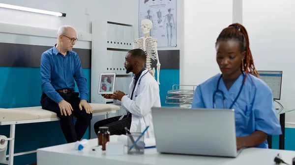 Medic showing cardiology diagnosis on digital tablet to old patient, explaining cadiogram and heart organ disease. Illustration of cardiovascular system test results to find healthcare treatment.