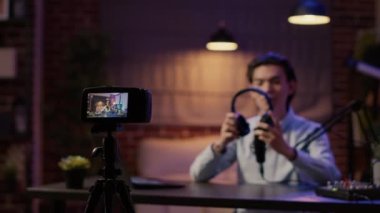 Camera recording video of vlogger doing product review with wireless headphones for channel content. Recommending audio headset on social media podcast episode, live broadcast show.