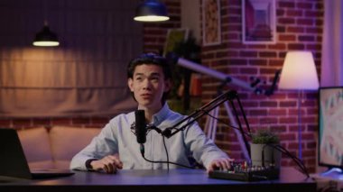 Male vlogger live broadcasting podcast episode on camera, using audio equipment. Creating content for social media channel and recording talk show video, web production. Tripod shot.