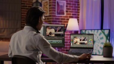 Graphic designer editing video montage on production software, working on computer to add visual effects and color grading on footage. Edit creative multimedia film with sound. Tripod shot.