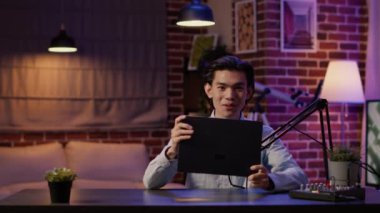 Asian man talking about laptop product and technology, doing review of wireless computer on podcast show. Vlogging pc recommendation for channel audience, live broadcast video.