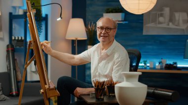 Sanatsal aletler ve ekipmanlarla profesyonel vazo başyapıtı çizen yaşlı kişinin portresi. Yaratıcılık becerilerini ve kalemleri kullanarak tuval üzerine tasarım modelinin çizimini yapmak.