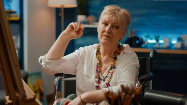 Fiziksel engelli bir kadın, sanatsal aletler ve yaratıcı yeteneklerle tuvale bir şaheser çiziyor. Vazo çizmek için kalem kullanan tekerlekli sandalye kullanıcısı..