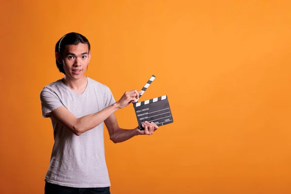 Clapper loader slapping slate, holding film making equipment, movie scene shooting. Cinematography, video production, young smiling asian cameraman assistant looking at camera