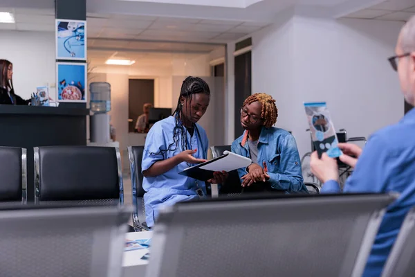 Health specialist taking notes at examination appointment with young patient, writing report papers to give healthcare insurance support in waiting room. Fillling in checkup form at cosultation.