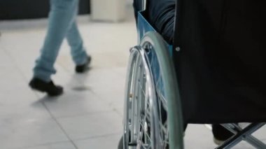 Retired person with physical impairment waiting in reception lobby to start checkup visit appointment with medic. Wheelchair user with disability in waiting room area at facility. Close up.