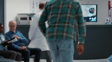 African american patient in waiting room area writing checkup report, talking to employee at hospital reception desk to attend medical appointment. Waiting in clinic lobby for consultation.