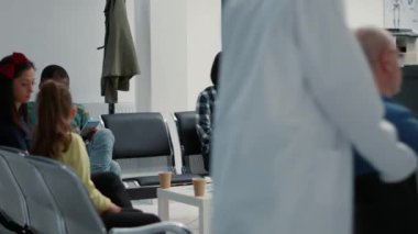 Asian patient filling in medical report at hospital reception lobby, sitting in waiting area to attend consultation appointment. Diverse patients waiting in healthcare facility.